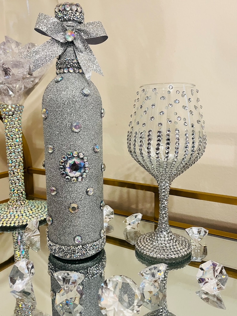 May include: A silver glitter wine bottle with a silver bow and rhinestones, and a silver glitter wine glass with rhinestones.
