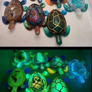 May include: A collection of nine resin turtle figurines, some with glitter and glow-in-the-dark features. The turtles are in various colors, including blue, green, brown, and gold. The turtles are arranged in two rows, with the top row showing the turtles in their regular colors and the bottom row showing the turtles glowing in the dark.
