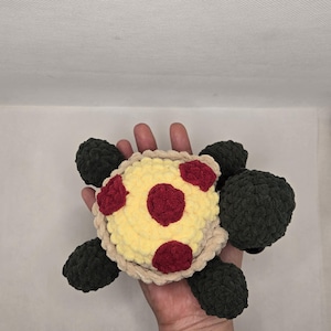 May include: A handmade crochet turtle toy. The turtle has a yellow shell with red spots, a tan border, and dark green flippers and head. The toy is soft and plush.