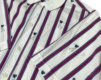 Puede incluir: Camisa de golf blanca con rayas verticales moradas y pequeños gráficos de jugadores de golf. La camisa tiene cuello blanco y cierre de botones. Las mangas son cortas. La camisa está hecha de un material ligero.