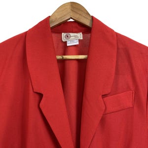 Può includere: Un blazer rosso con scollo a V e chiusura con un solo bottone. Il blazer ha un'etichetta che recita "Vero Moda London".