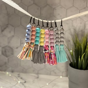 May include: A set of eight colorful beaded keychains with fabric tassels. The beads are pastel blue, pink, yellow, and green. The tassels are a variety of patterns and colors.