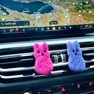 May include: Two felt car air fresheners shaped like Peeps, one pink and one blue, hanging from the air vent of a car.