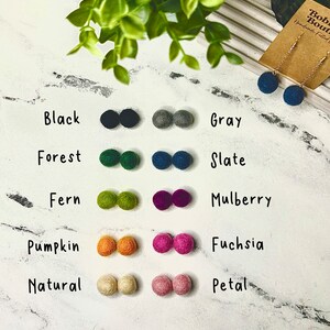 Op de afbeelding: Viltbal oorbellen en viltballen in diverse kleuren, waaronder zwart, grijs, bosgroen, leisteenblauw, varengroen, moerbei, pompoen, fuchsia, naturel en bloembladroze. Er is ook een paar leisteenblauwe oorbellen te zien.
