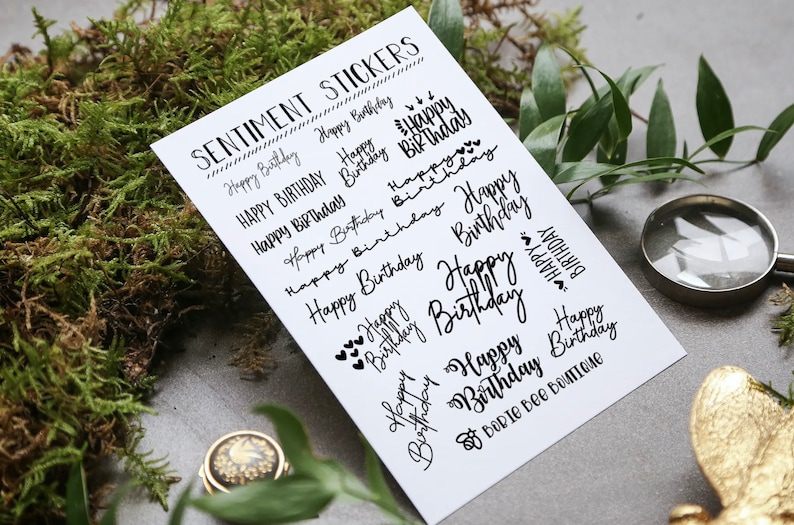 Puede incluir: Una hoja de papel blanco con texto negro que dice "Sentiment Stickers" y presenta varios mensajes escritos a mano de "Feliz cumplea&ntilde;os". Las pegatinas est&aacute;n dise&ntilde;adas para manualidades y scrapbooking.