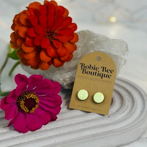 May include: A pair of light green glitter stud earrings on a brown card with the text "Bobie Bee Boutique Handmade Wooden Earrings" and the website address "www.BobieBeeBoutique.com".