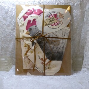 May include: A brown paper package tied with a brown ribbon. The package contains a set of paper cutouts for a craft project. The cutouts are of a rooster, a chicken, and a rooster head. The package is labeled "Daisy Kingdom Country Kitchen Collection".