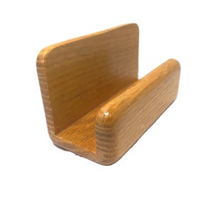May include: A wooden napkin holder with a U-shaped design. The holder is made of light brown wood with a glossy finish. The holder is designed to hold napkins upright on a table or counter.