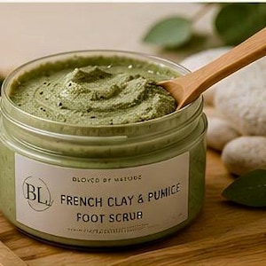 Peut inclure: Un pot en plastique transparent rempli d'un gommage pour les pieds vert clair à la texture épaisse. L'étiquette blanche porte l'inscription BL, BLOVED BY NATURE, FRENCH CLAY & PUMICE FOOT SCRUB. Une cuillère en bois est insérée dans la pâte.