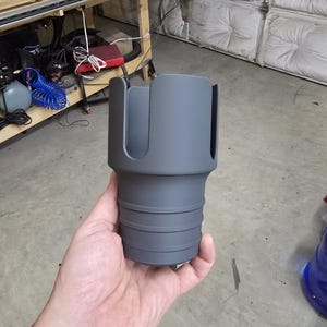 Könnte beinhalten: Ein grauer Plastik-Becherhalter mit einer strukturierten Oberfläche und einem gerippten Boden. Der Becherhalter ist so konzipiert, dass er einen Becher sicher hält.