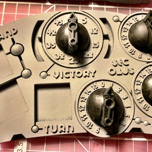 May include: A gray plastic game board with four square spaces, labeled "Command", "Victory", "Turn", and "Sec Plus".  There are three black dials with numbers and arrows, each with a black knob.