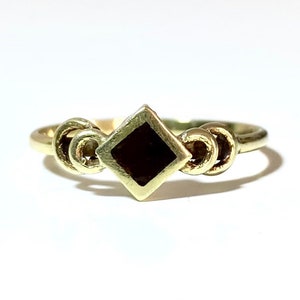 May include: A gold ring with a black square stone set in the center. The band of the ring is decorated with three interlocking circles.