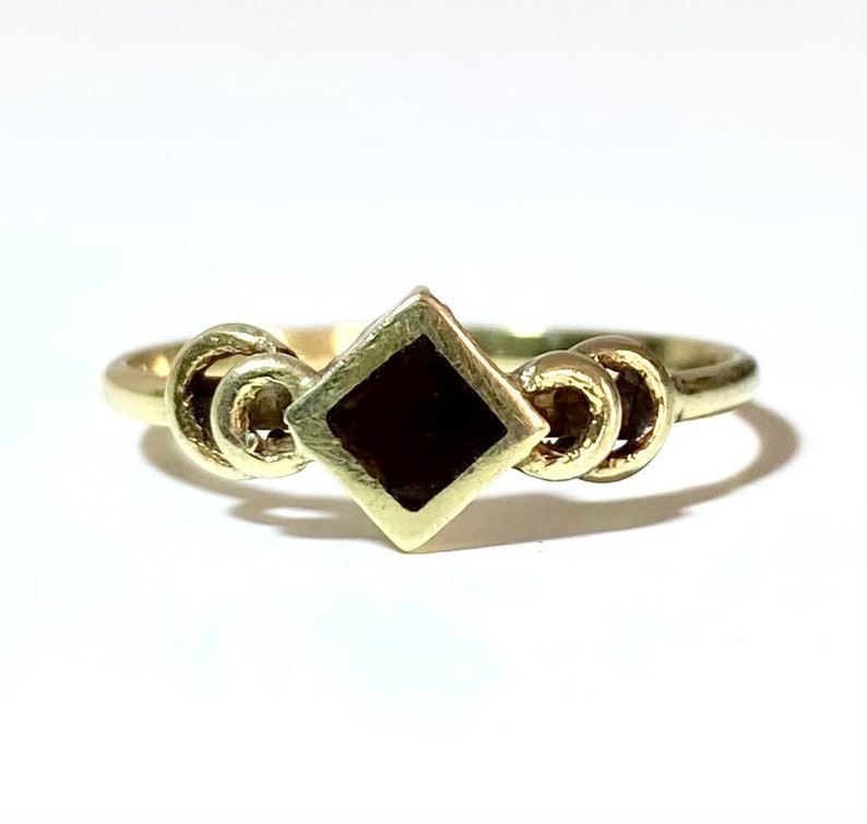 May include: A gold ring with a black square stone set in the center. The band of the ring is decorated with three interlocking circles.