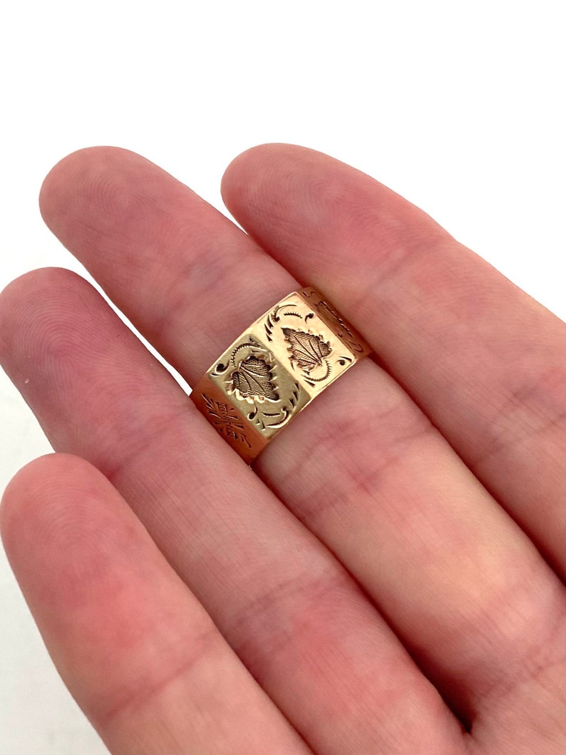 May include: A gold band ring with an intricate floral design. The ring is worn on a person's finger.