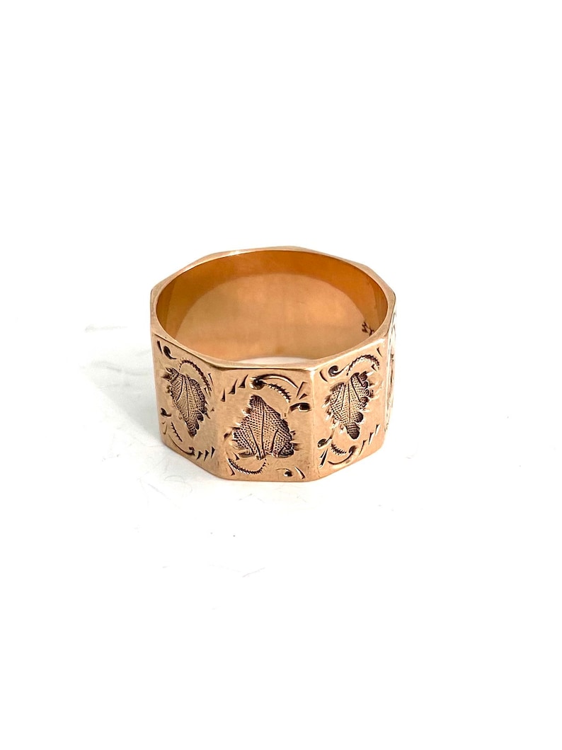 May include: A gold ring with an octagonal band and a detailed engraved design of leaves and swirls.