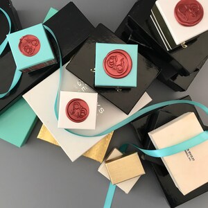 May include: A stack of small, black, white, and turquoise boxes with red wax seals. The boxes are decorated with gold and silver accents. The boxes are labeled "Jewelry" and "Gifts".