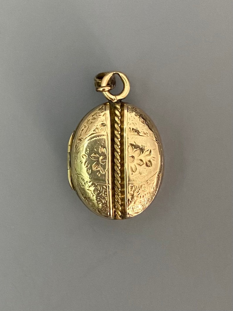 May include: A gold oval locket with a rope-like design down the center and floral engravings on the front.
