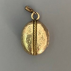 May include: A gold oval locket with an intricate engraved design. The locket has a hinged opening and a loop for attaching a chain.