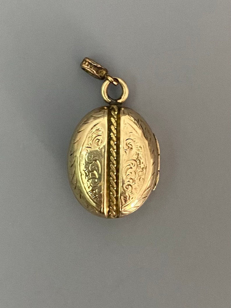 May include: A gold oval locket with an intricate engraved design. The locket has a hinged opening and a loop for attaching a chain.