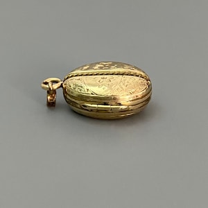 May include: A gold locket pendant with an intricate floral design. The locket is closed and has a small loop for attaching a chain.