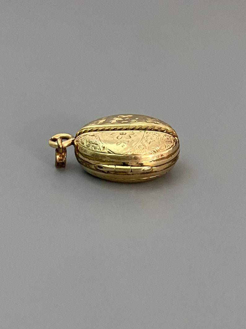 May include: A gold locket pendant with an intricate floral design. The locket is closed and has a small loop for attaching a chain.
