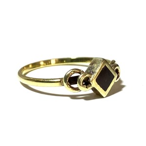 May include: A gold ring with a black square stone set in the center. The ring has a decorative design on the band.