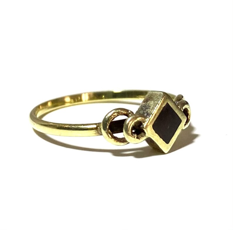 May include: A gold ring with a black square stone set in the center. The ring has a decorative design on the band.