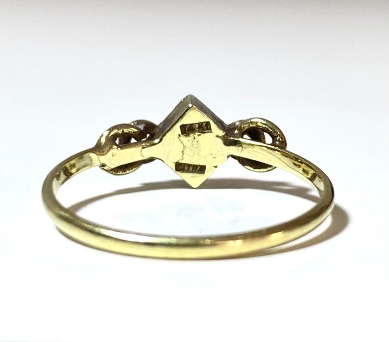 May include: A gold ring with a square-shaped gemstone in the center and two smaller gemstones on either side.