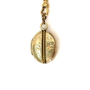 May include: A gold locket with a chain attached. The locket is oval shaped and has an intricate floral design.