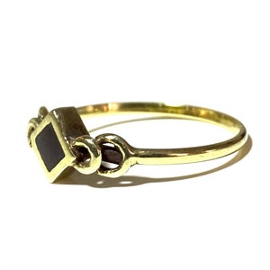 May include: A gold ring with a black square-shaped stone set in the center. The ring has a decorative design on the band.