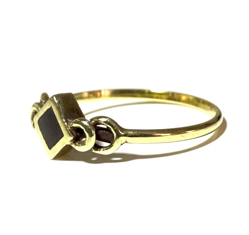 May include: A gold ring with a black square-shaped stone set in the center. The ring has a decorative design on the band.