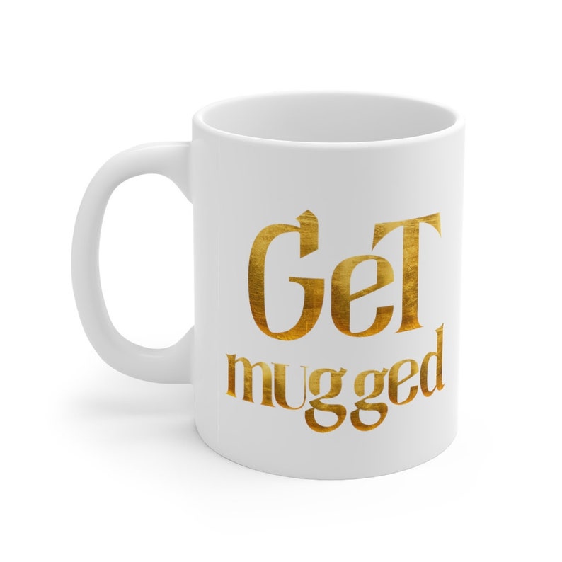 Puede incluir: Taza de cer&aacute;mica blanca con un dise&ntilde;o met&aacute;lico dorado que dice "Get mugged".