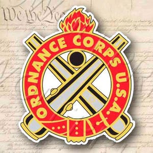 May include: A red, white, and black Ordnance Corps U.S.A. emblem with a crossed cannon design and a flaming torch.