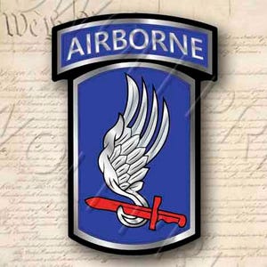 May include: A blue and silver military patch with the word "AIRBORNE" in white letters on a silver banner. The patch features a white stylized wing with a red dagger.