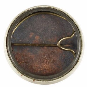 K&ouml;nnte beinhalten: Ein runder, alter Knopf mit wei&szlig;em Rand und rostbraunem Innenraum. Die R&uuml;ckseite zeigt eine Messingnadel und einen Verschluss zum Befestigen. Das Design des Knopfes deutet darauf hin, dass es sich um einen &auml;lteren Artikel handelt, m&ouml;glicherweise ein Sammlerst&uuml;ck oder ein Erinnerungsst&uuml;ck.
