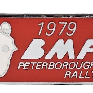 May include: A red and silver pin with the text "1979 BMF PETERBOROUGH RALLY". The pin features a white silhouette of a motorcycle and rider. The pin is diamond-shaped with a silver border.