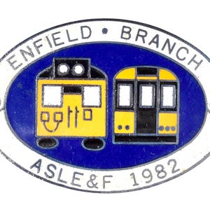 May include: An oval-shaped pin featuring two yellow train cars on a blue background, with the words "ENFIELD BRANCH" and "ASLE&F 1982" in white lettering. The pin has a white border.