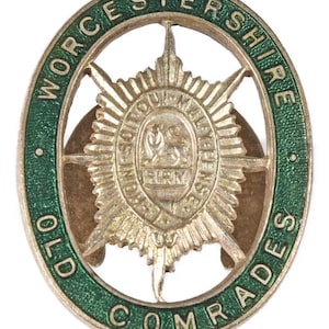 Könnte beinhalten: Ein Vintage-Metallabzeichen mit grünem Rand und dem Text "WORCESTERSHIRE OLD COMRADES" am Rand. In der Mitte befindet sich ein Sternmuster mit einem Wappen und den Worten "IN SOUTOU MALYENSIS". Das Abzeichen hat eine ovale Form.