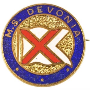May include: A vintage pin with a gold border and a blue outer ring. The pin features the text "M.S. DEVONIA" in gold lettering. The center design includes a red "X" shape over a white and gold background.