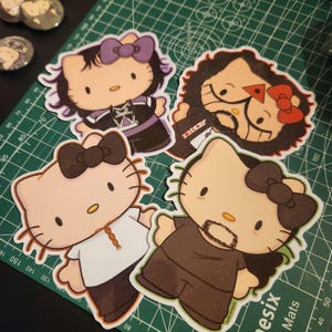 May include: Four Hello Kitty stickers with different characters. Each sticker features a Hello Kitty character with a different hairstyle and facial hair. The stickers are on a green cutting mat.