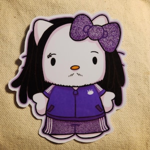 Puede incluir: Una pegatina de Hello Kitty morada y blanca con un bigote blanco y negro, que lleva un chándal morado con rayas blancas y una huella de pata blanca en el pecho.