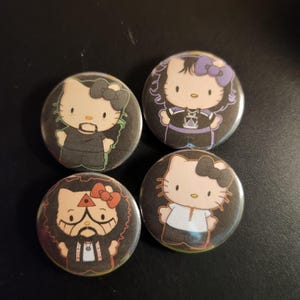 May include: Four round buttons featuring different Hello Kitty characters. Each character is dressed in a unique outfit and has a distinct expression. The buttons are black, white, purple, and green.