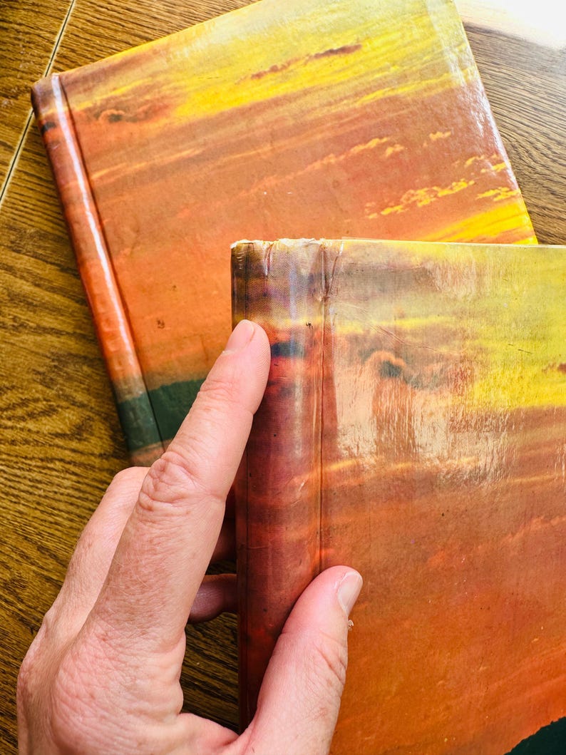 May include: Two hardback books with orange, yellow and red sunset-like covers. The books are stacked on top of each other.