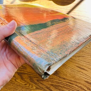 May include: Close-up of the spine of a hardback book with a sunset scene on the cover. The title "Picturesque" is visible on the spine.