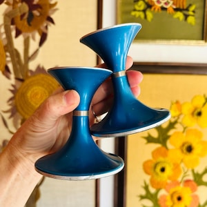 May include: Two teal blue candle holders with silver trim. The holders are shaped like a wide, inverted cone.