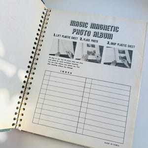 May include: A black and white photo album with a gold spiral binding. The cover has the text "Magic Magnetic Photo Album" and instructions for using the album: "1. Lift Plastic Sheet 2. Place Photo 3. Drop Plastic Sheet". The album has an index page with lines for writing in.