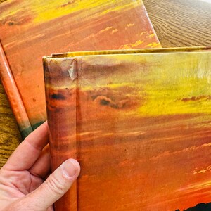 May include: Two hardback books with a sunset scene on the cover. The books are stacked on top of each other. The top book is slightly askew.