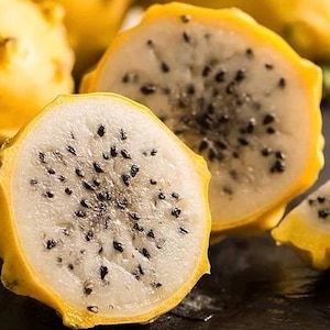 May include: A close-up of a halved yellow dragon fruit, revealing white flesh dotted with black seeds. The fruit's skin is a vibrant yellow, and the interior is a creamy white. The image highlights the fruit's unique texture and color contrast.