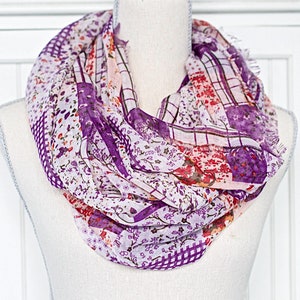 May include: A white, purple, and orange patterned infinity scarf. The scarf is made of a soft, lightweight fabric and is perfect for adding a touch of color to any outfit.