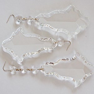 May include: Three clear glass crystal chandelier prisms with a faceted design and a silver hook.